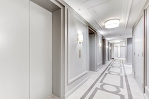 Ein Hotelgang mit Türen auf beiden Seiten, Leuchten an der Decke und einem gemusterten Teppich.