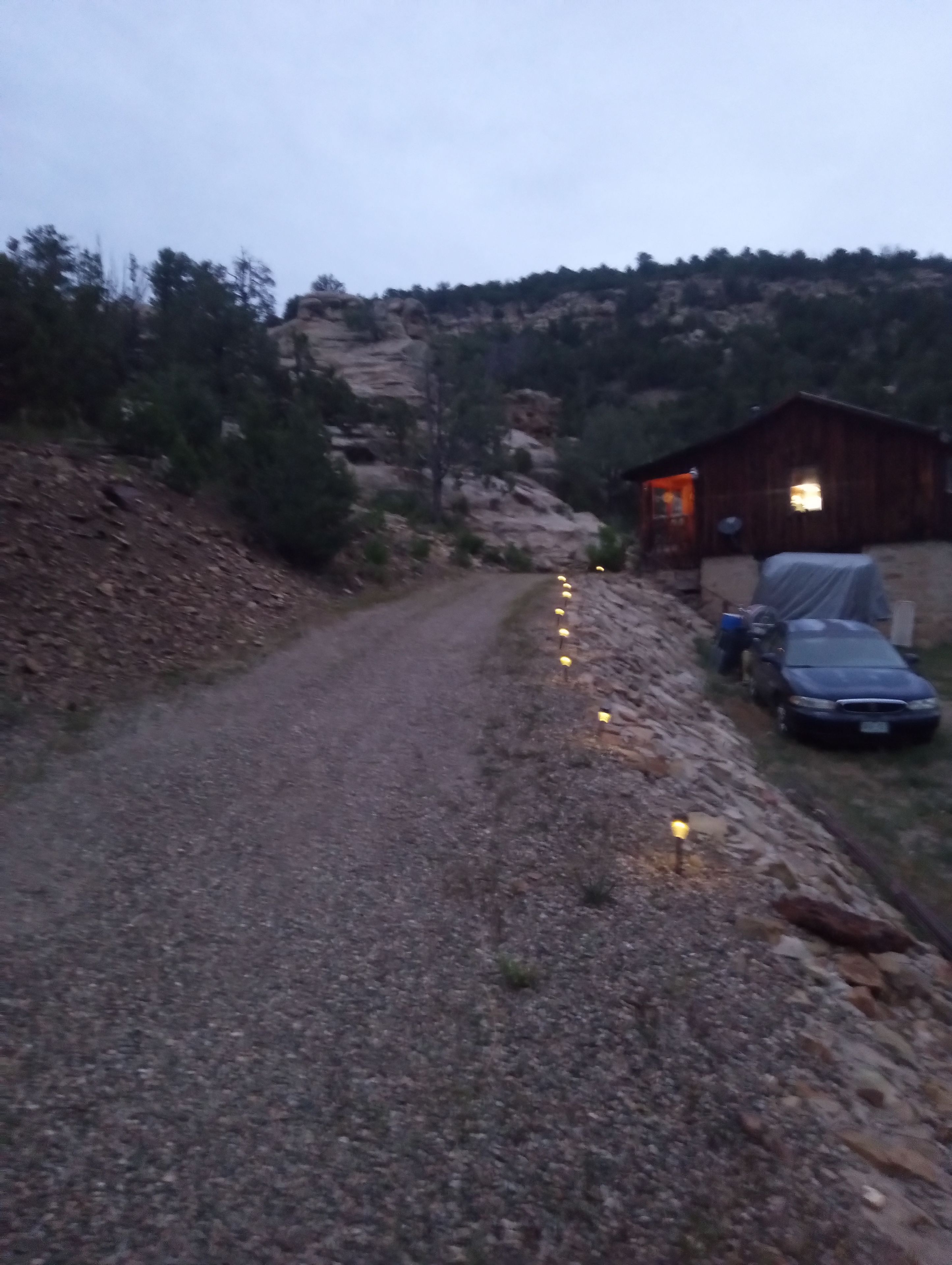 A gravel road leading to a wooden cabin with a car parked nearby.