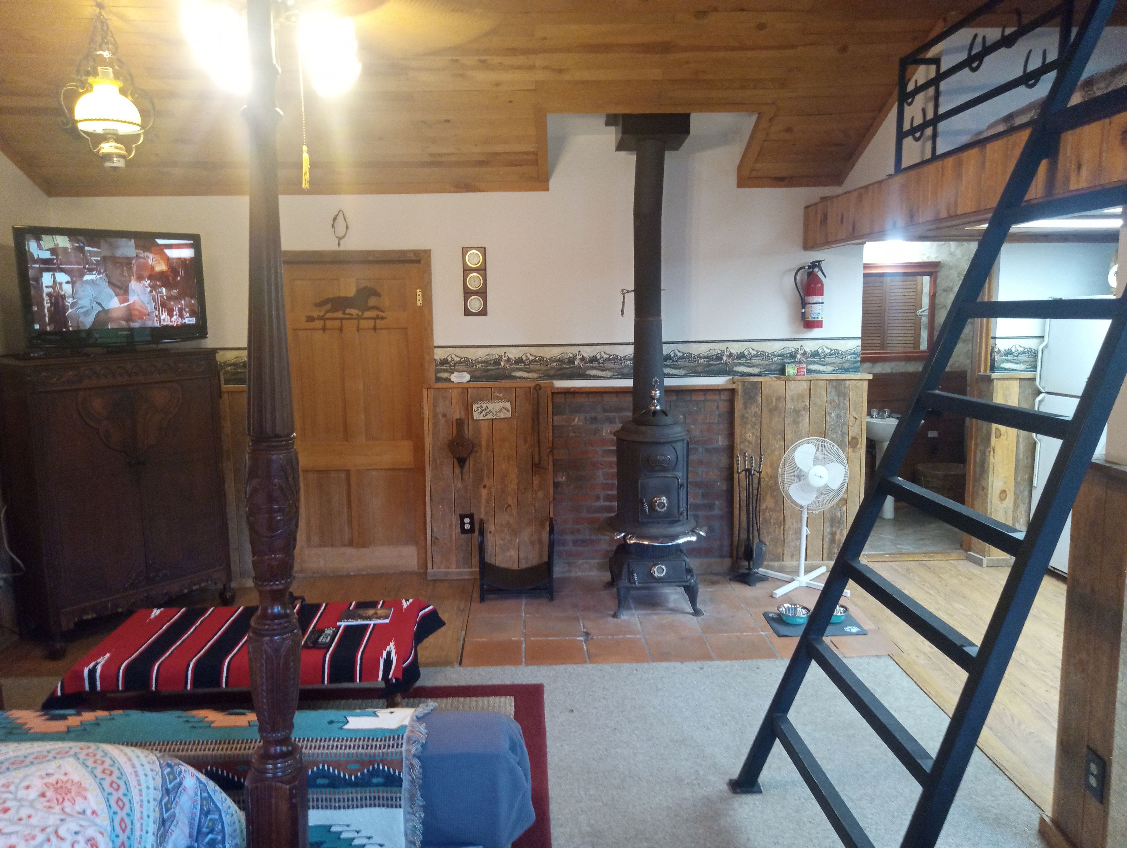 A rustic interior with a wooden ceiling, a fireplace, a television, and a ladder.