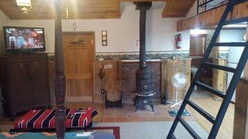 A rustic interior with a wooden ceiling, a fireplace, a television, and a ladder.