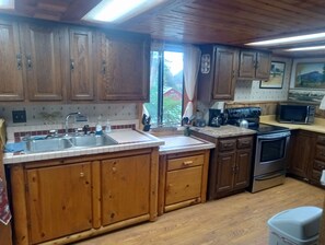 Una cocina con armarios de madera, un lavamanos de acero inoxidable, un microondas y una estufa.