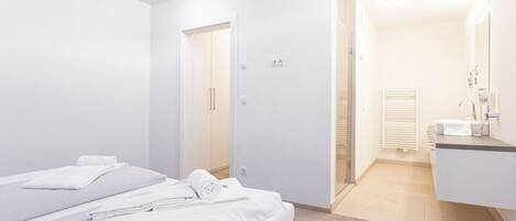 A modern hotel room with a bed, a bathroom with a sink and mirror, and a walk-in closet.