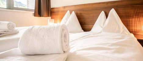 A hotel room with a neatly made bed, a rolled white towel, and a blue object on the bed.