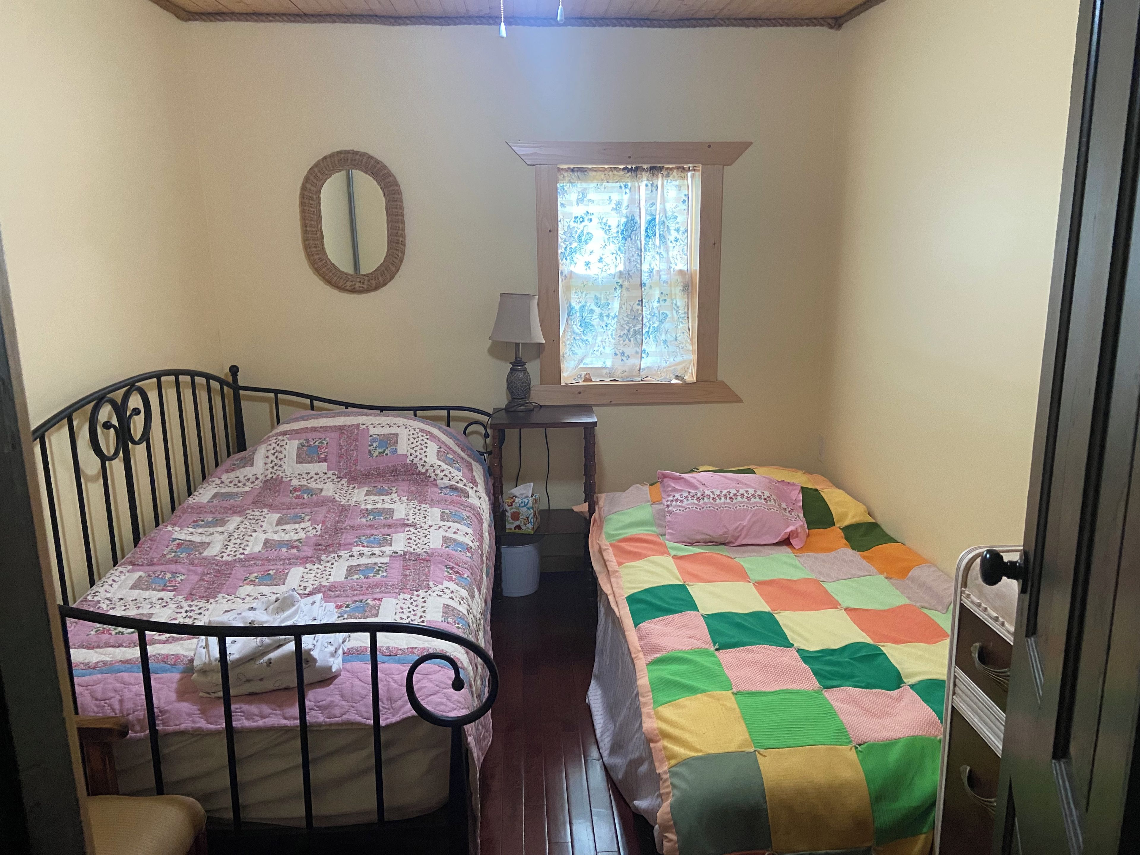 A room with two beds, a window with curtains, a mirror, and a lamp.