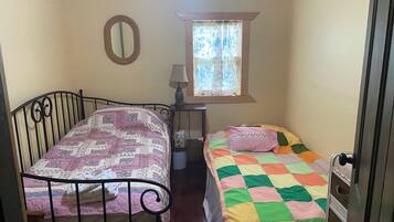 A room with two beds, a window with curtains, a mirror, and a lamp.