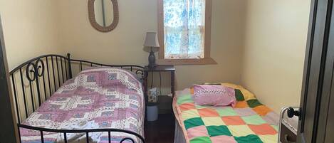 Una habitación con dos camas, una ventana con cortinas, un espejo y una lámpara.