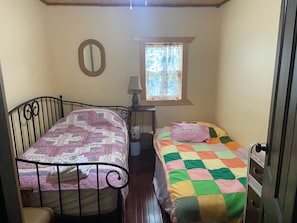 A room with two beds, a window with curtains, a mirror, and a lamp.