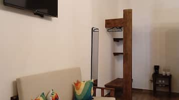 Ein Wohnzimmer mit einer Couch, einem Flachbildfernseher, einer hölzernen Bank und einem kleinen Tisch mit einer Kaffeemaschine.