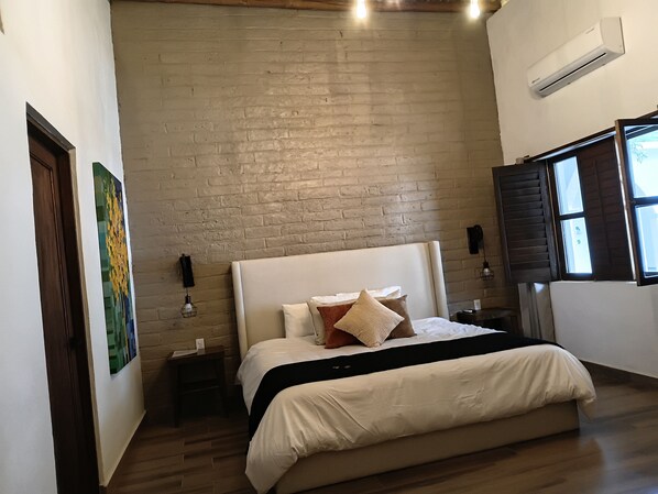A bedroom with a brick wall, a bed with white bedding, a nightstand, and a window with blinds.
