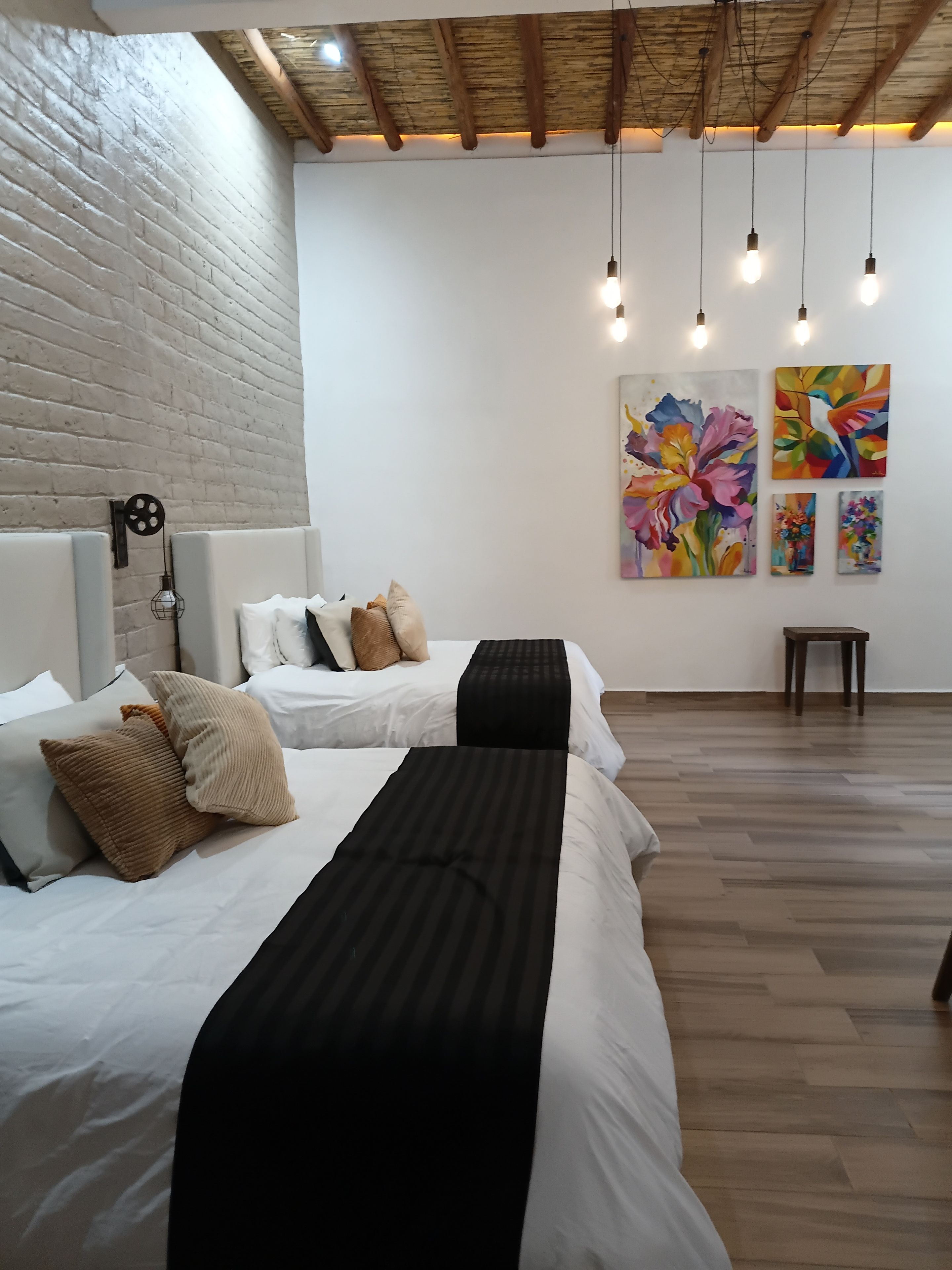Ein modernes Schlafzimmer mit zwei Betten, einer Ziegelwand, Holzbalken an der Decke und Bildern an der Wand.