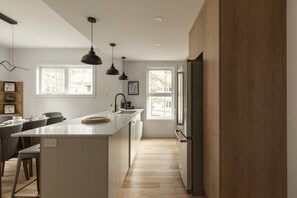 A modern kitchen with a central island, pendant lighting, and a view to the outside. - Bright Condo | Bike+ Randos In/Out • Vue Montagne (Les Laurentides Regional County Municipality)