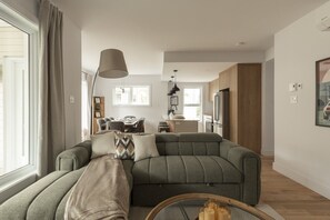 Ein modernes Wohnzimmer mit einer Eckcouch, einem Essbereich und einer Küche im Hintergrund.