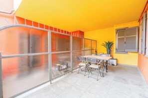 Ein Zimmer mit Glastrennwand, einem Tisch mit Stühlen, einer Topfpflanze und einem Fenster mit Rollläden.
