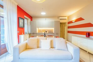 Una sala de estar moderna con un sofá blanco, una cocina al fondo y una pared a rayas rojas y blancas.