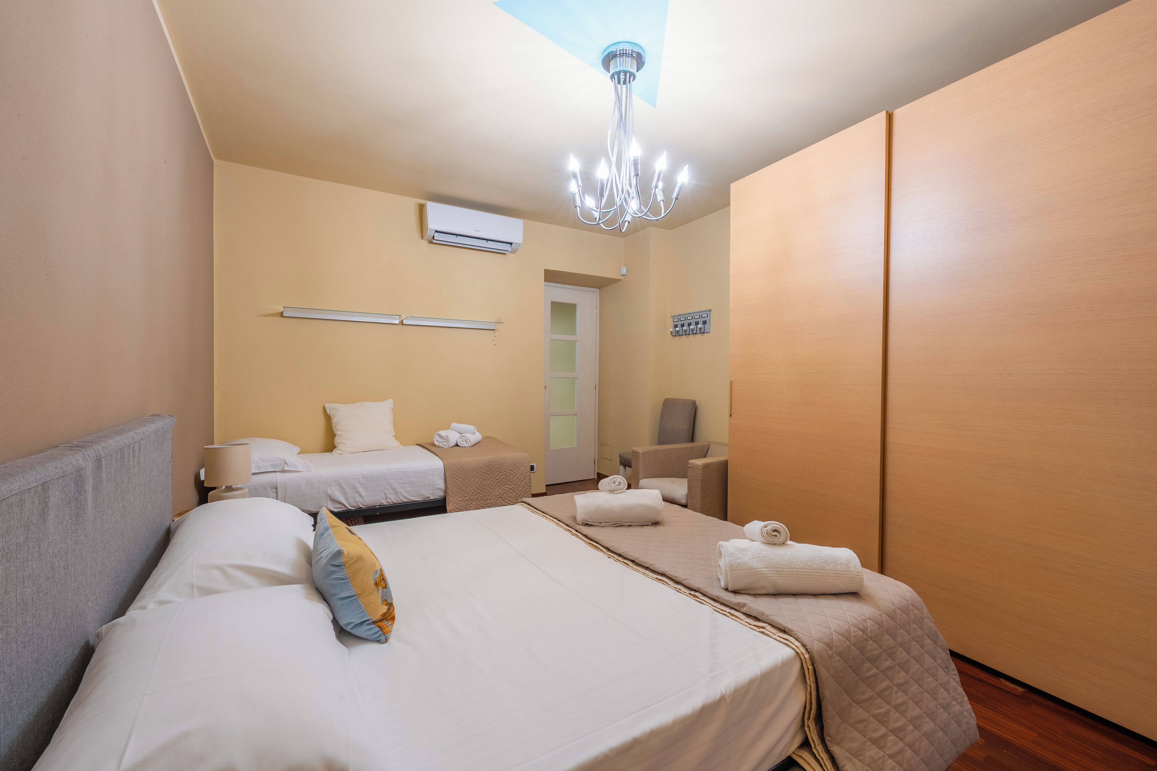 Ein Hotelzimmer mit zwei Betten, einer Kristallleuchter, einer Klimaanlage, einem Handtuchhalter und einer Tür.