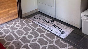 A laundry room with a washing machine, a dryer, and a rug with text.