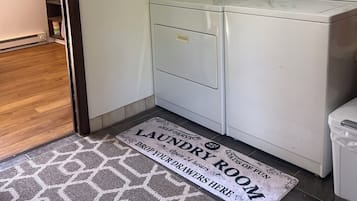 Een wasserette met een wasmachine, een droger en een vloerkleed met tekst.