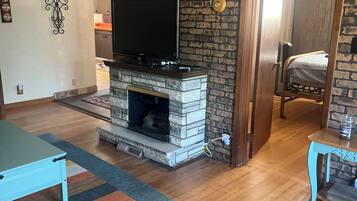 Een woonkamer met een open haard, een televisie en een kleurrijk gestreept tapijt.