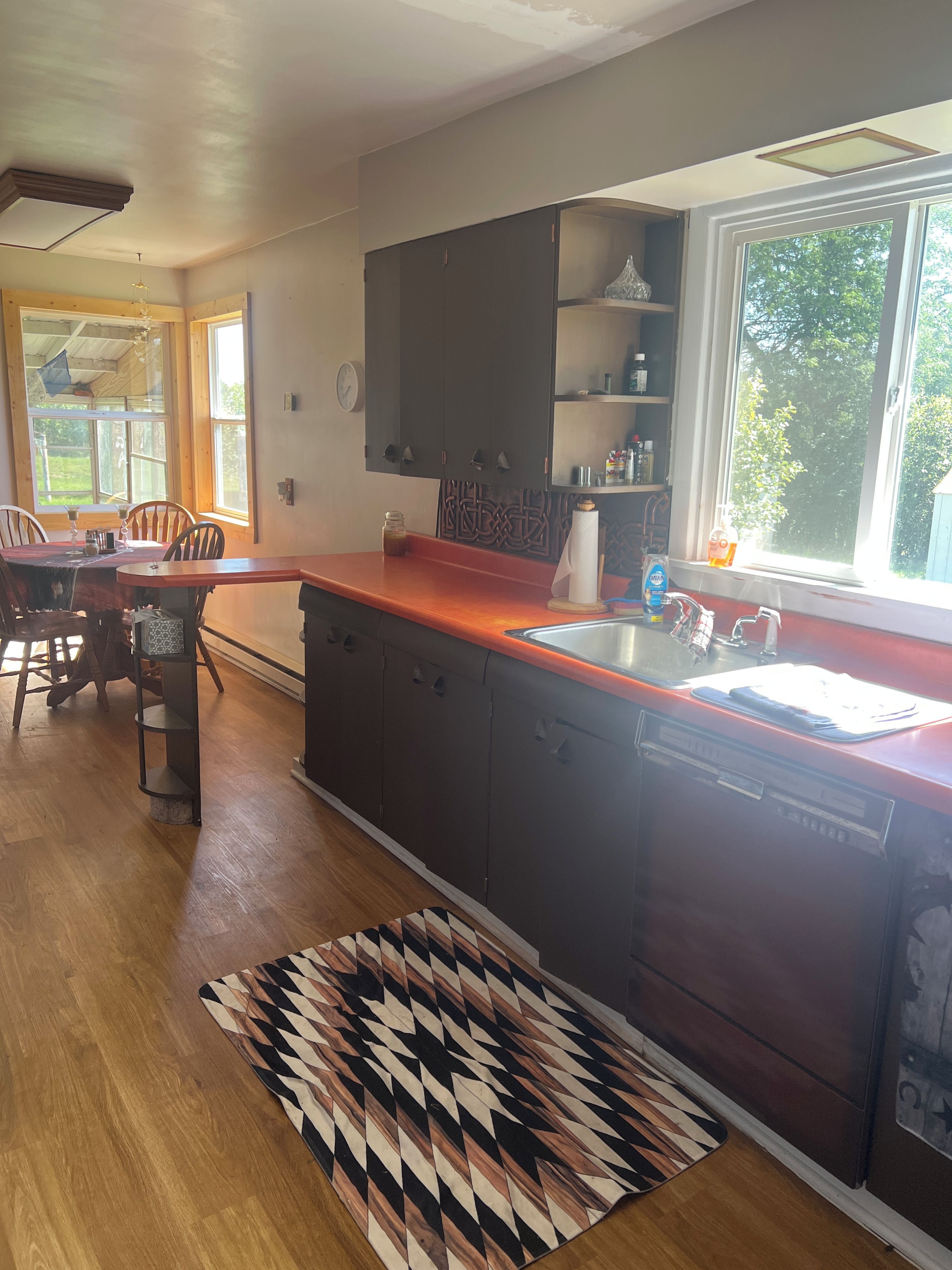 A kitchen with wooden cabinets, a red countertop, a built-in sink, and a patterned rug.