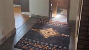 A hallway with a patterned rug leading to a room with a window and curtains.