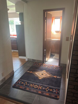 A hallway with a patterned rug leading to a room with a window and curtains.