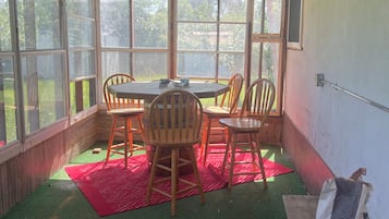 Een kamer met een tafel, stoelen, een rode mat en een grill op de vloer.