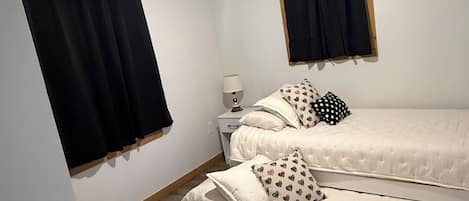 Un dormitorio con una cama individual, una mesita de noche, un ventilador de techo y cortinas negras.
