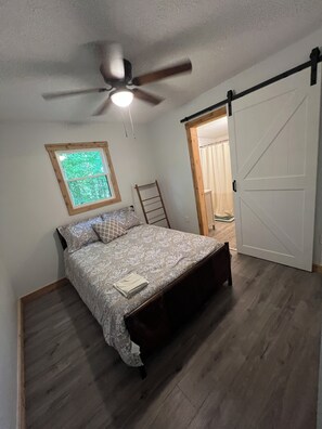 A bedroom with a bed, a ceiling fan, a window, and a door. - Nolin Lake Woodland O-Asis with Golf Cart (Mammoth Cave)