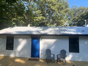 A single-story house with a blue door, two windows, and a porch with two Adirondack chairs. - Nolin Lake Woodland O-Asis with Golf Cart (Mammoth Cave)