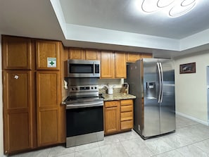 A kitchen with wooden cabinets, stainless steel appliances including a microwave, oven, and refrigerator, and a granite countertop. - Home Sweet Home: 4-Bed, 3-Bath – Pet Friendly (Las Vegas)