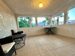 A room with a tiled floor, a table, a chair, and a window with a view of palm trees and buildings. - Home Sweet Home: 4-Bed, 3-Bath – Pet Friendly (Las Vegas)