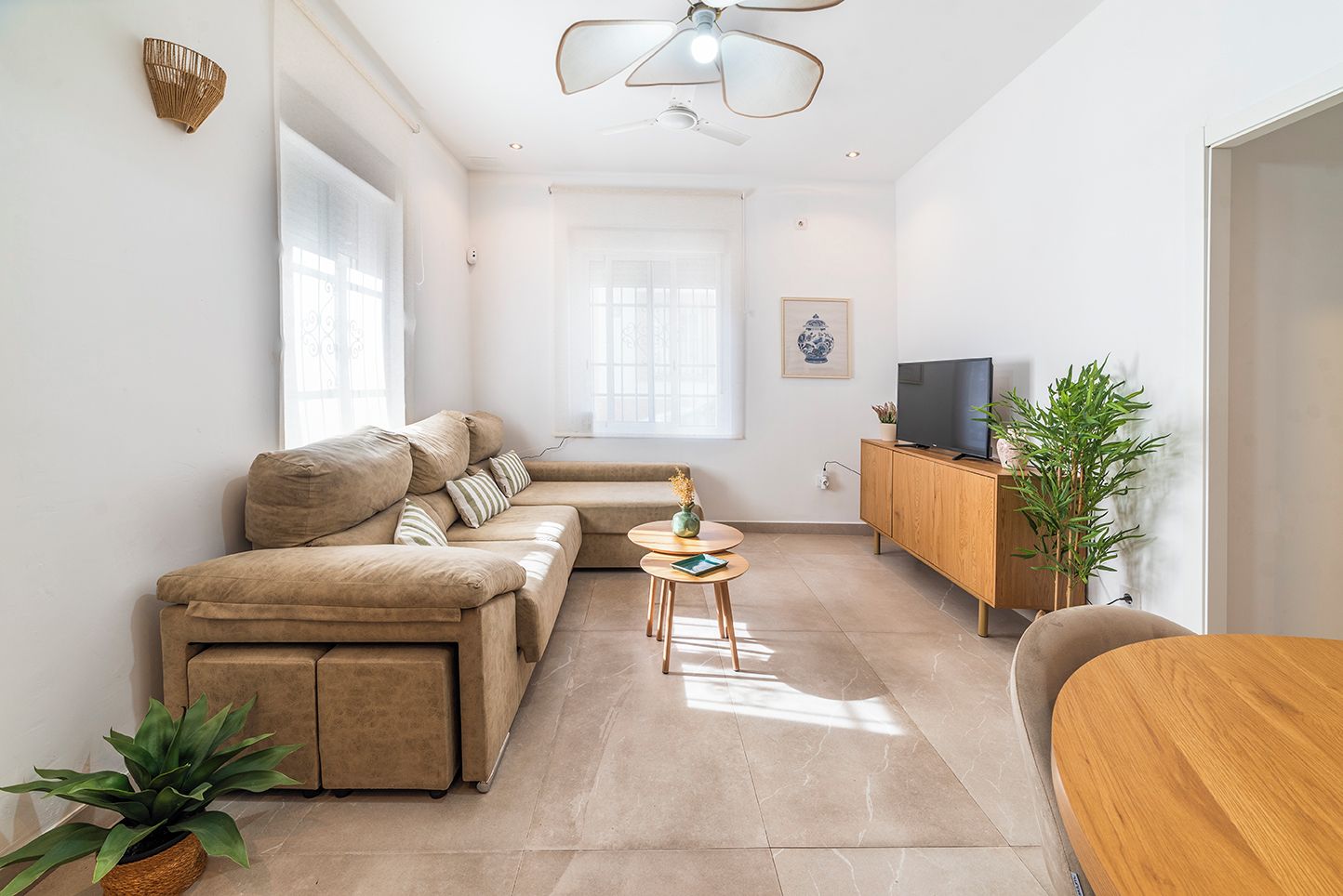 Ein modernes Wohnzimmer mit einer Couch, einem kleinen runden Tisch, einem Fernseher auf einer Holzkommode und einer Pflanze.