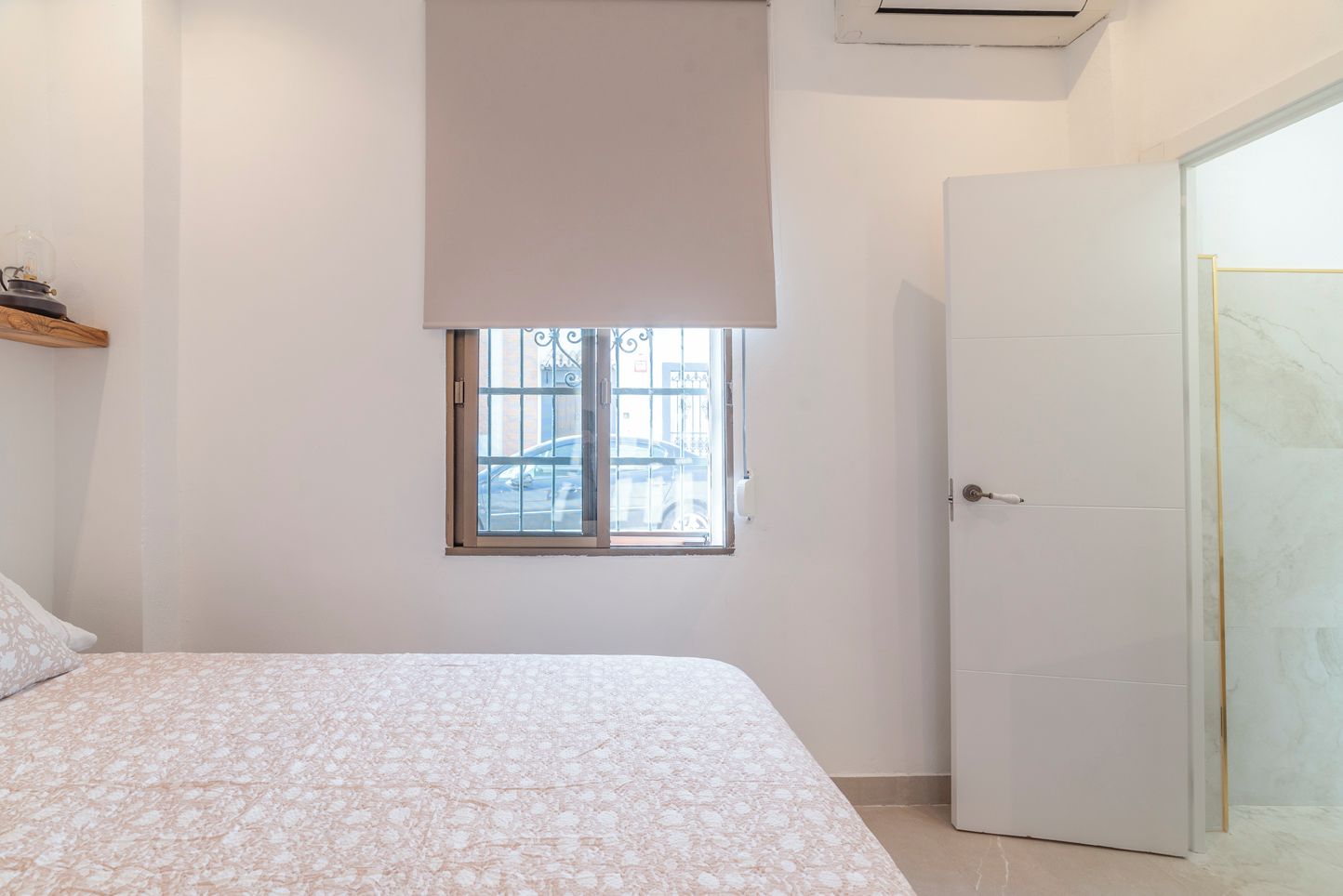 Een slaapkamer met een bed, een raam met uitzicht op geparkeerde auto's, en een gesloten deur.