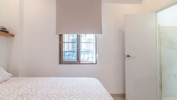 Een slaapkamer met een bed, een raam met uitzicht op geparkeerde auto's, en een gesloten deur.