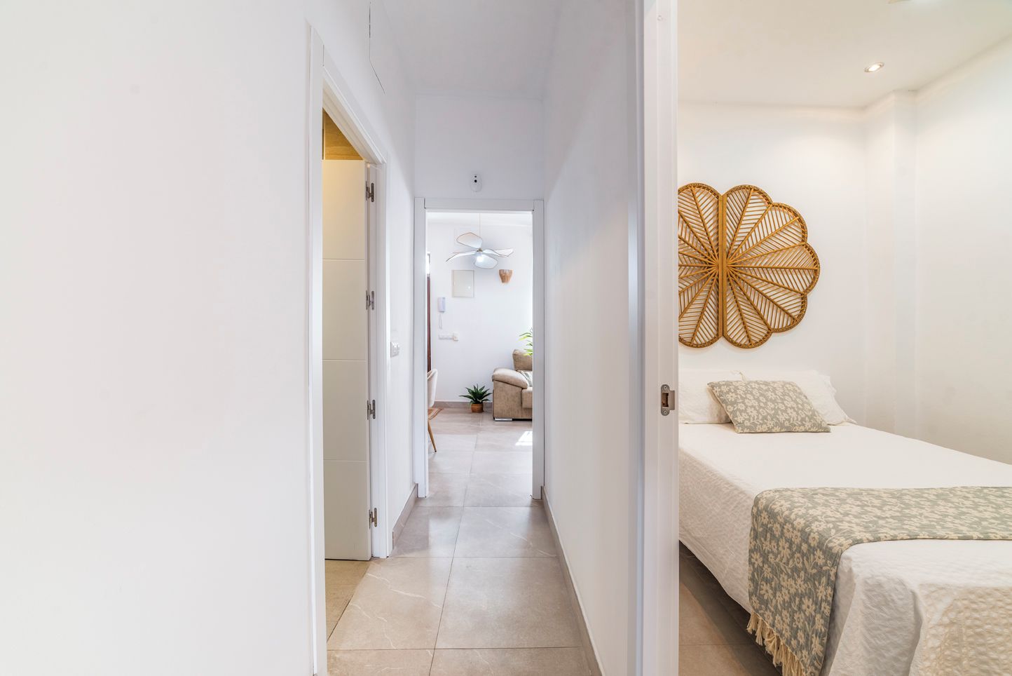 A hotel room with a bed, a bedside table, a wall-mounted decorative item, and a view into the adjacent room.