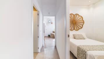 A hotel room with a bed, a bedside table, a wall-mounted decorative item, and a view into the adjacent room.