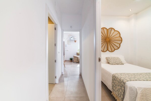 A hotel room with a bed, a bedside table, a wall-mounted decorative item, and a view into the adjacent room.