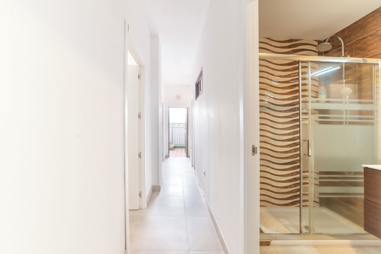 A hallway with a glass shower enclosure and a view of a garden.