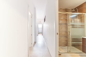 A hallway with a glass shower enclosure and a view of a garden.