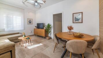 Een moderne woonkamer met een bank, een eettafel met stoelen, een televisie op een houten kast en een plafondventilator.