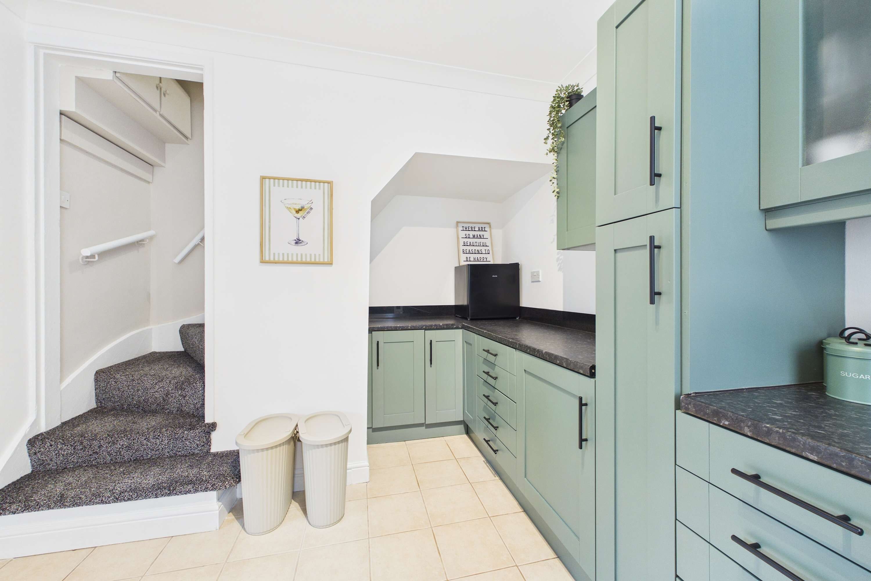 A kitchen with light green cabinets, a black refrigerator, and a framed picture on the wall.
