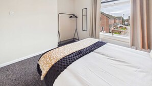 Een hotelkamer met een bed, een raam met gordijnen, een hanglamp en uitzicht op buiten.