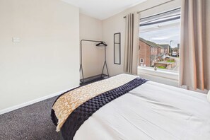 A hotel room with a bed, a window with curtains, a hanging light, and a view of the outside. - South Kirkby Home | Sleeps 6 | Parking (South Kirkby)