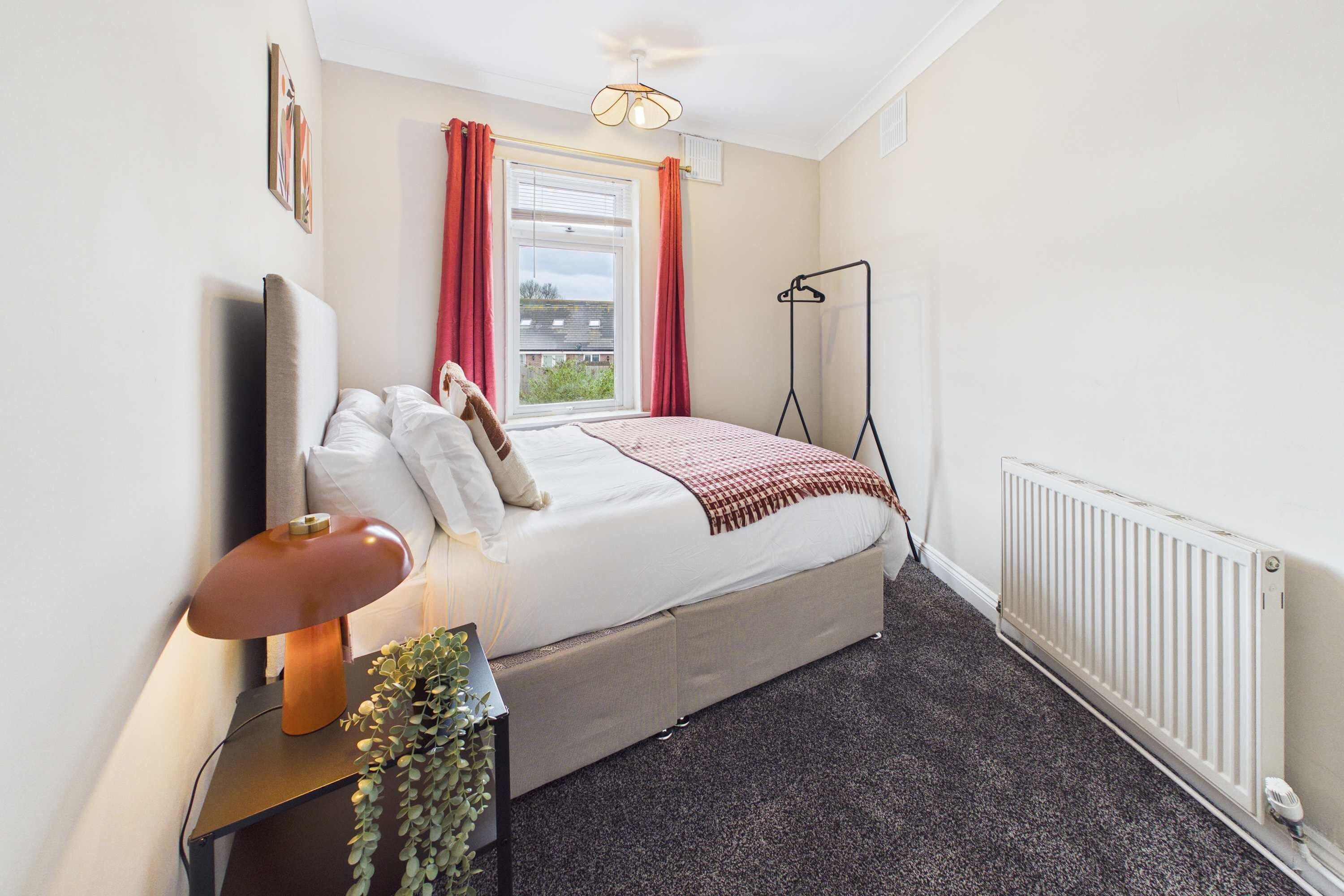 A bedroom with a bed, bedside table, lamp, and a radiator.