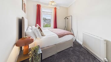 A bedroom with a bed, bedside table, lamp, and a radiator.