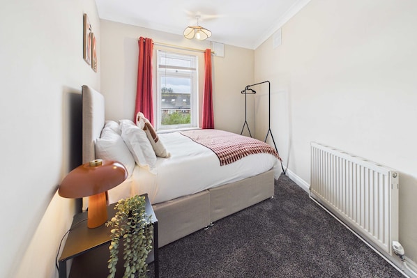 Une chambre à coucher avec un lit, une table de chevet, une lampe et un radiateur.