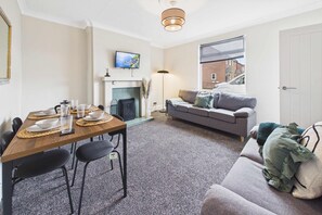 A living room with a fireplace, a dining area with a table set for four, and a sofa with cushions. - South Kirkby Home | Sleeps 6 | Parking (South Kirkby)