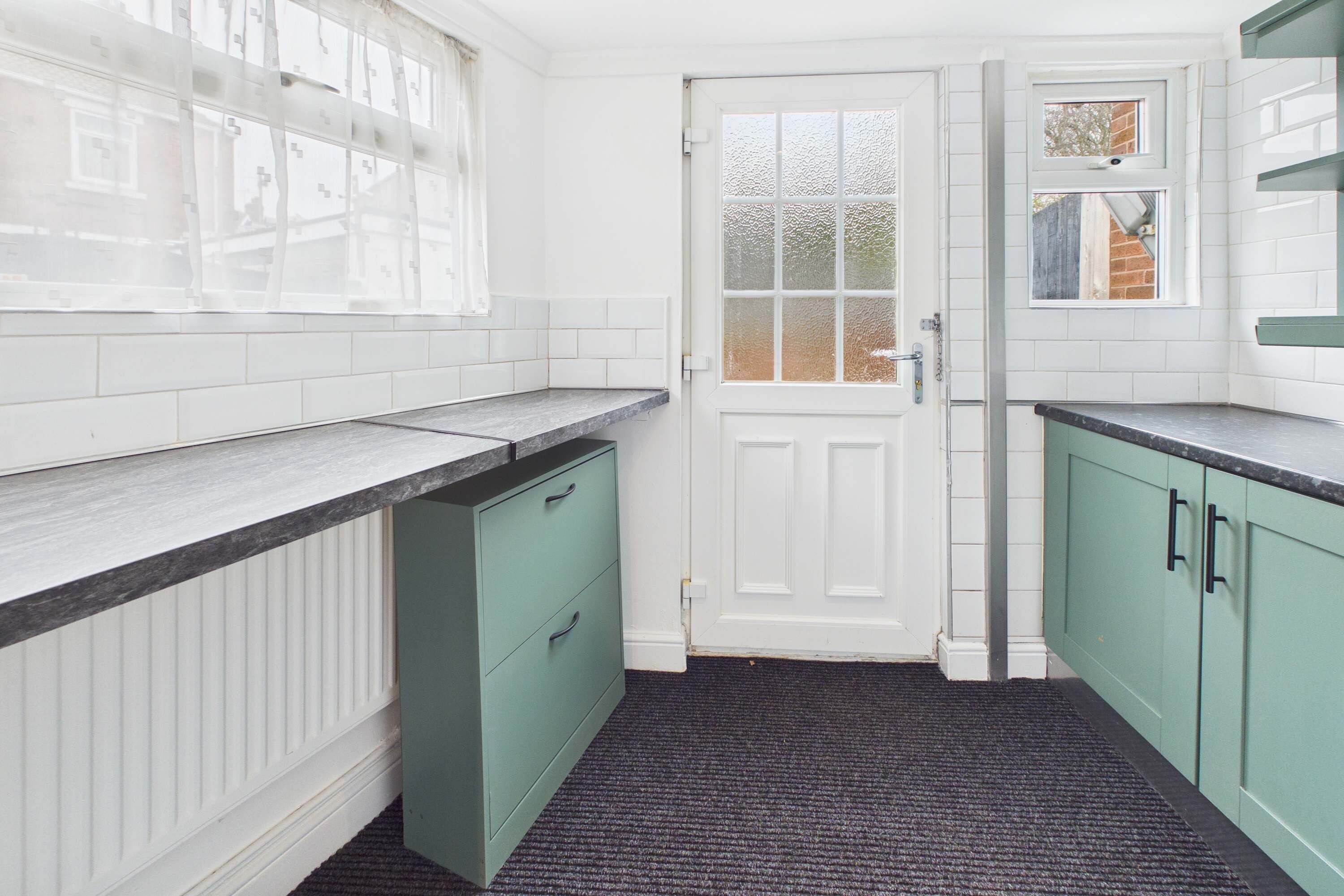 A kitchen with white tiled walls, a white door, and green cabinets.