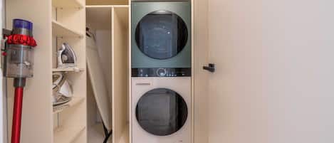 Un cuarto de lavandería con lavadora y secadora, un aspirador y estantes con productos de limpieza.