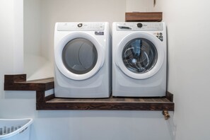 Two front-loading washing machines on a wooden shelf in a laundry room. - The Powder Den (Revelstoke)